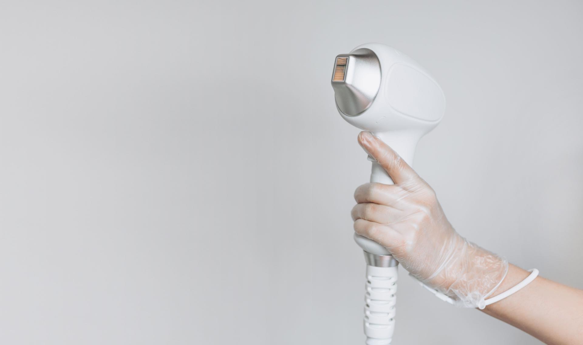 Laser device for removing unwanted hair in the hand of nurse. Laser hair removal, cosmetic body treatments. Concept of hygiene, beauty, health. Girl holding a working part of the epilator in her hand