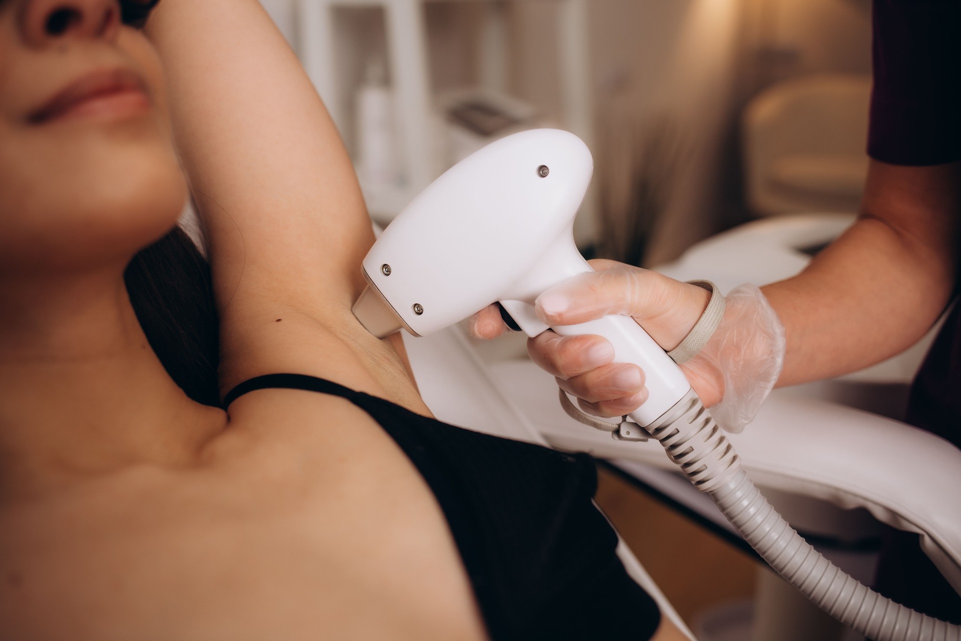 Body care concept. Laser hair removal. Young Caucasian woman in safety glasses lies on the sofa, female cosmetologist doing laser hair removal in a beauty salon