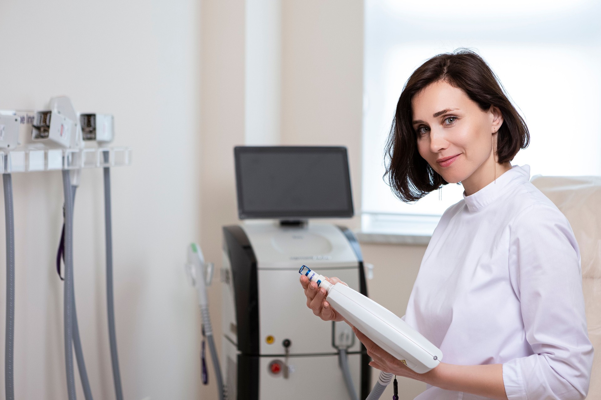 Medicine Concepts. Professional Confident Female Laser Skin Treatment Professional  Doctor Posing in Doctor's Smock With Laser Medical Equipment in Beauty Salon.